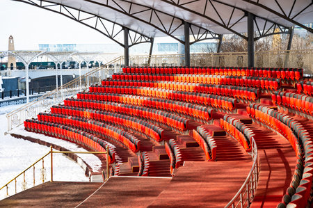 Red seats in an empty outdoor auditorium covered by a canopy. The snow-dusted surroundings enhance...