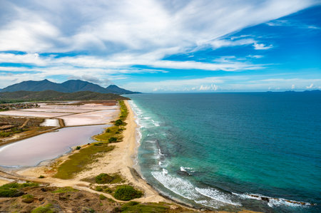 A breathtaking aerial view captures the vibrant salt flats alongside the pristine coastline and mountains of Venezuela. The vivid contrast between land and sea creates a stunning natural landscape.の写真素材