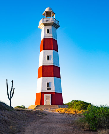 Lighthouse on Margarita Island stands tall against a vivid blue sky. The sandy beach and green vegetation create a serene landscape, perfect for travel and nature photography.の写真素材