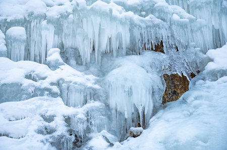 Breathtaking view of an icy waterfall in the Argun Gorge during winter. Cascading frozen water creates a natural sculpture against a rocky cliff, showcasing nature's frozen beauty.の写真素材