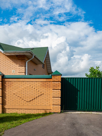 Brick house featuring a sturdy green metal gate and a matching fence. Captivating contrast of brickwork with vibrant green elements adds distinct charm to the home exterior.の写真素材