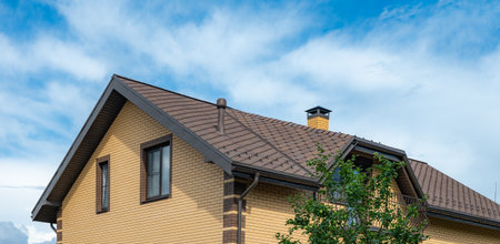 Brick house with sophisticated tile roofing and a prominent chimney. The architectural design showcases a modern, elegant appearance with large windows and detailed craftsmanship.の写真素材