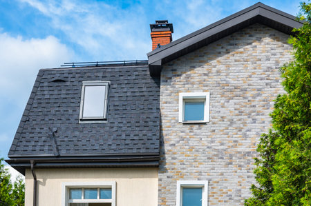 Brick house with sophisticated tile roofing and a prominent chimney. The architectural design showcases a modern, elegant appearance with large windows and detailed craftsmanship.の写真素材