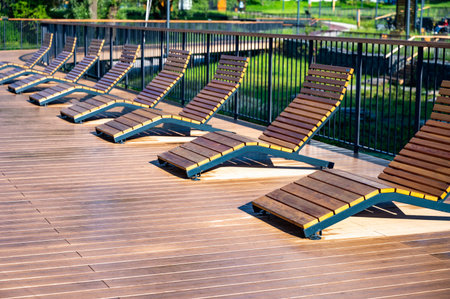 Empty wooden lounge chairs line an outdoor deck, set against a lush green park backdrop. The scene is serene and peaceful, capturing stillness.の写真素材