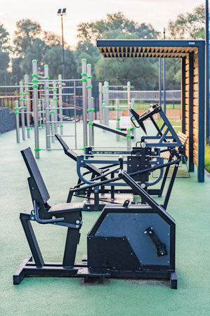 Outdoor gym equipment in a park offering fitness options for the public. Various machines and structures for strength training and cardio exercises are set on a sunny day.の写真素材