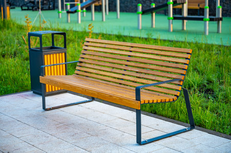 Empty wooden park bench surrounded by lush green grass. Sunlight filters through the foliage, creating a peaceful and serene outdoor setting in a public park.の写真素材
