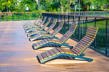 Empty wooden lounge chairs line a wet outdoor deck after rain, set against a lush green park backdrop. The scene is serene and peaceful, capturing stillness after a downpour.の写真素材