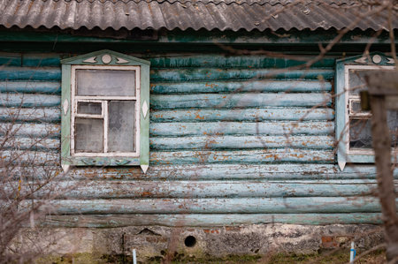 Old wooden house facade with two windows, displaying a rustic charm with peeling turquoise paint and...