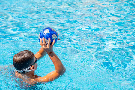 Young sporty boy playing ball in big outdoor swimming pool with tranquil waterの写真素材