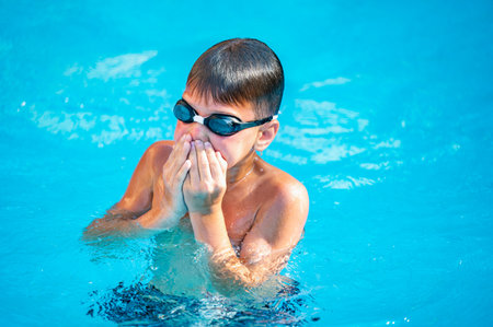 happy boy swimming in the pool, wearing goggles and swim trunksの写真素材