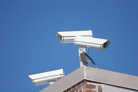 Three security cameras on top of building against blue sky