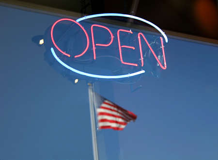 Shop window with neon open sign and American flag reflectionの写真素材