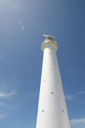 A white lighthouse rising into the blue sky against the sunの写真素材