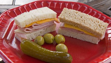 Ham and cheese finger sandwiches on a red plate with a pickle and olivesの写真素材
