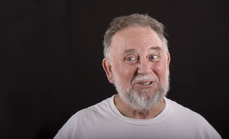 An older man in white tshirt looking to the right against black backgroundの写真素材