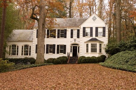 A nice white two story house with leaves covering the lawnの写真素材