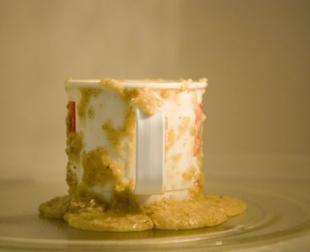 A cup running over with hot oatmeal in a microwave ovenの写真素材