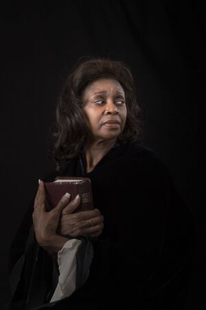 A woman holding a bible to her chest and looking to the left on black backgroundの写真素材