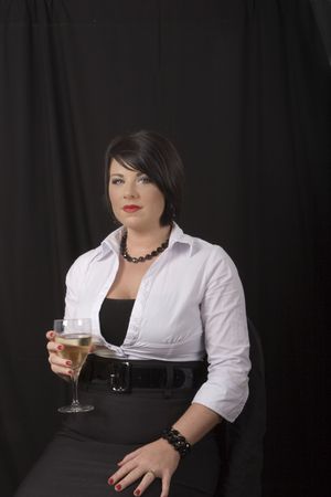 A model with black hair and white blouse sitting in a chair with a glass of wine on a black backgroundの写真素材