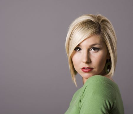 A blonde model with highlights in her hair in green blouse on grey background looking at cameraの写真素材