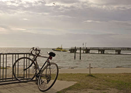 A bicycle on a rack with a pier and a pilot boat in the backgroundの写真素材