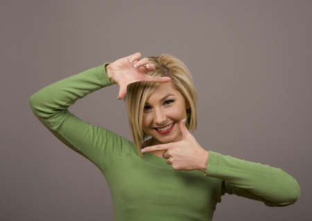 A blonde fashion model in green blouse framing her face with her handsの写真素材