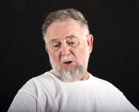 An old man in a white tshirt against a black background with an expression of woe or sadnessの写真素材