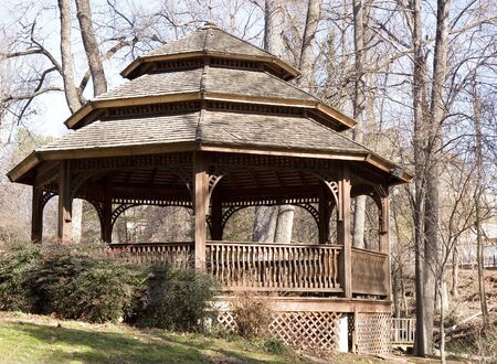 A large wooden gazebo in the yard of a farm house against a backdrop of winter trees and blue skyの写真素材