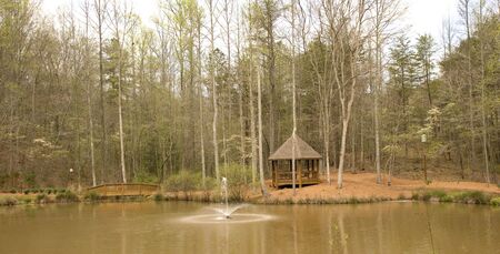 A nice wood gazebo on the shore of a lake with a fountainの写真素材