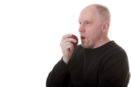 An older guy in a black shirt on a white background enjoying a healthy snack of a fresh red appleの写真素材