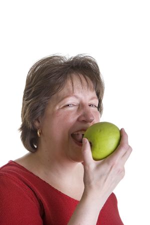 A middle aged woman in red smiling and eating a green appleの写真素材