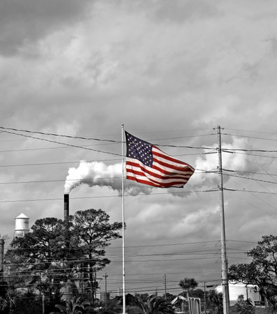 An American flag blowing in the wind in front of an industrial plantの写真素材