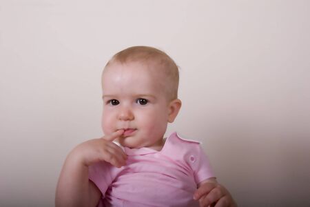 A baby in pink with dark eyes and finger on mouth on grey backgroundの写真素材