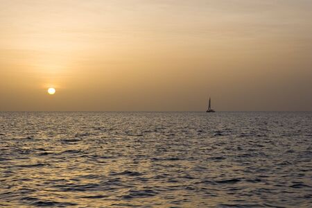 A sailboat on the horizon at sunsetの写真素材