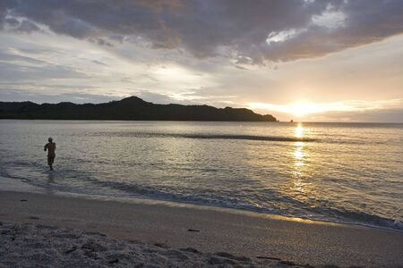 A man fishing on the beach as the sun setsの写真素材