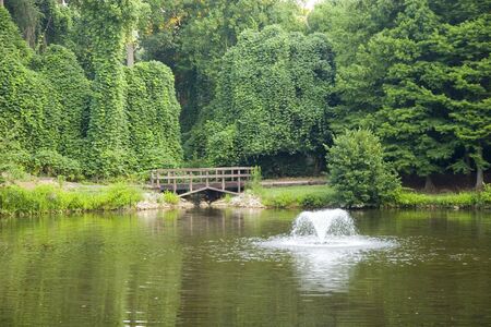 A fountain and an old wooden bridge on a small lakeの写真素材