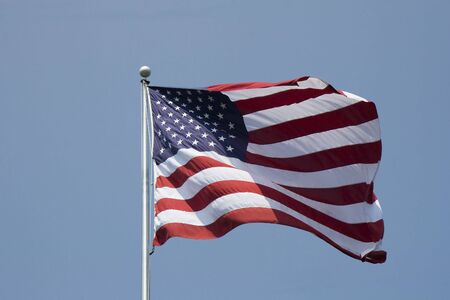 An American flag waving in the wind against a blue skyの写真素材