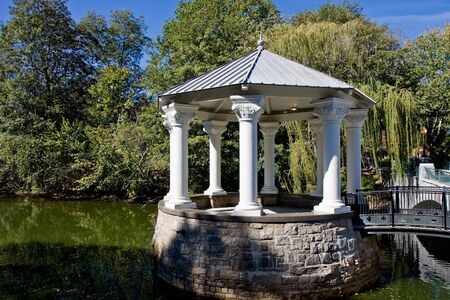 A stone and wood columned gazebo on a peaceful lakeの写真素材