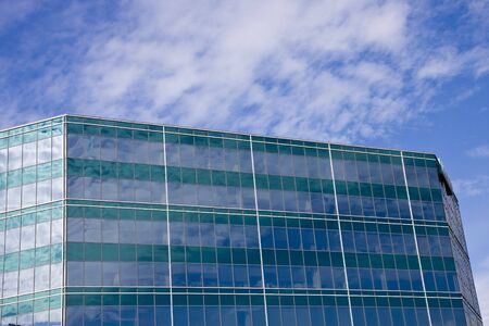 A green and blue glass building with sky and clouds reflectedの写真素材