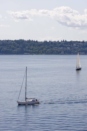 Two sailboats in a calm bay; one under sail, one under motorの写真素材