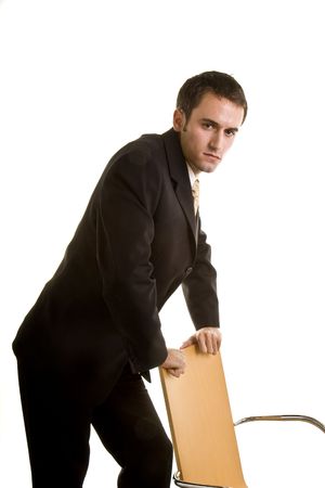 A  young man in a business suit leaning against a chair with a serious expressionの写真素材