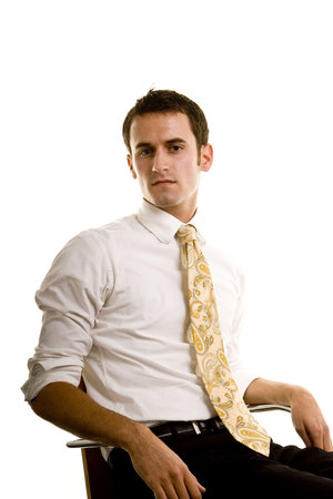 Young man wearing dress shirt and tie, sitting in a chair looking at the camera