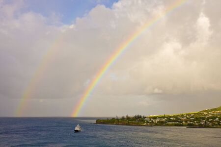 A ferry sailing past a tropical island under a rainbowの写真素材