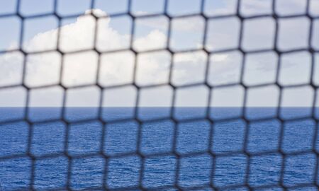 A rope mesh fence in front of the oceanの写真素材