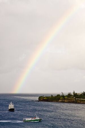Two ferries cruising between islands under an early morning rainbowの写真素材