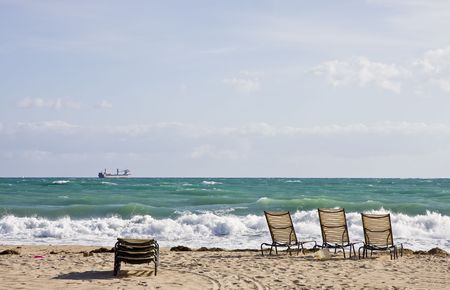Chaise Lounges on an empty beach under cloudy skies with a freighter out to seeの写真素材