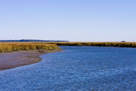 A wetlands marsh with a salt water channel and crystal blue skyの写真素材