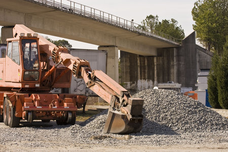 A large loader and a gravel pile under a rapid rail bridge