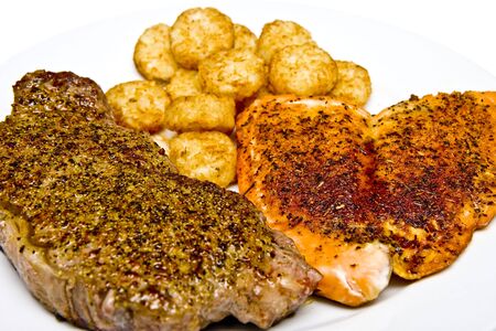Steak, Salmon, and potato puffs on a white plateの写真素材