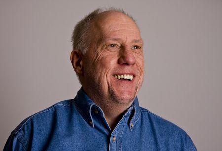 An older bald man in a blue shirt on a grey backgroundの写真素材
